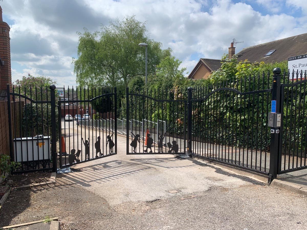 A black wrought iron gate is open to a driveway.