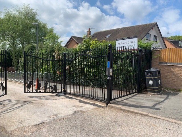 A black fence is surrounding a house with a trash can in front of it.