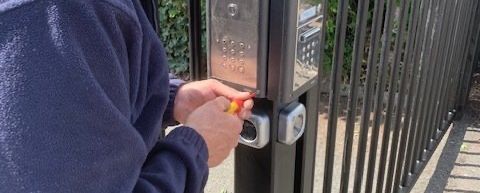 A man is using a screwdriver to fix a gate lock.