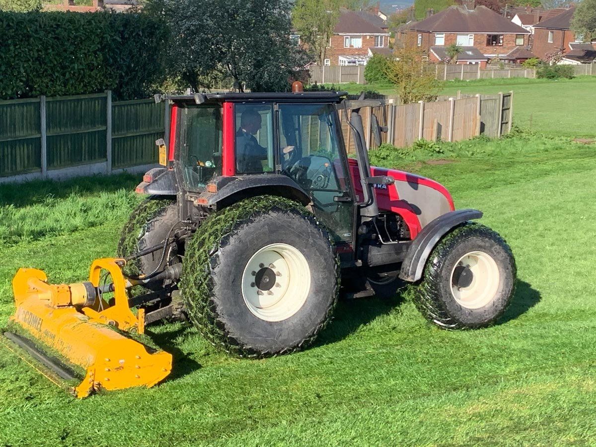 A tractor is cutting grass in a field with a yellow mower attached to it.