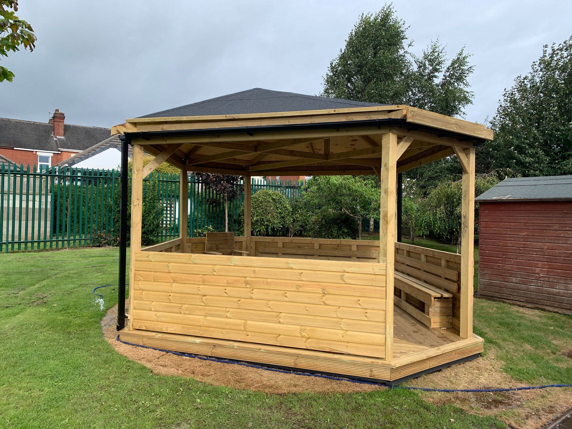 A wooden gazebo is sitting in the middle of a lush green field.