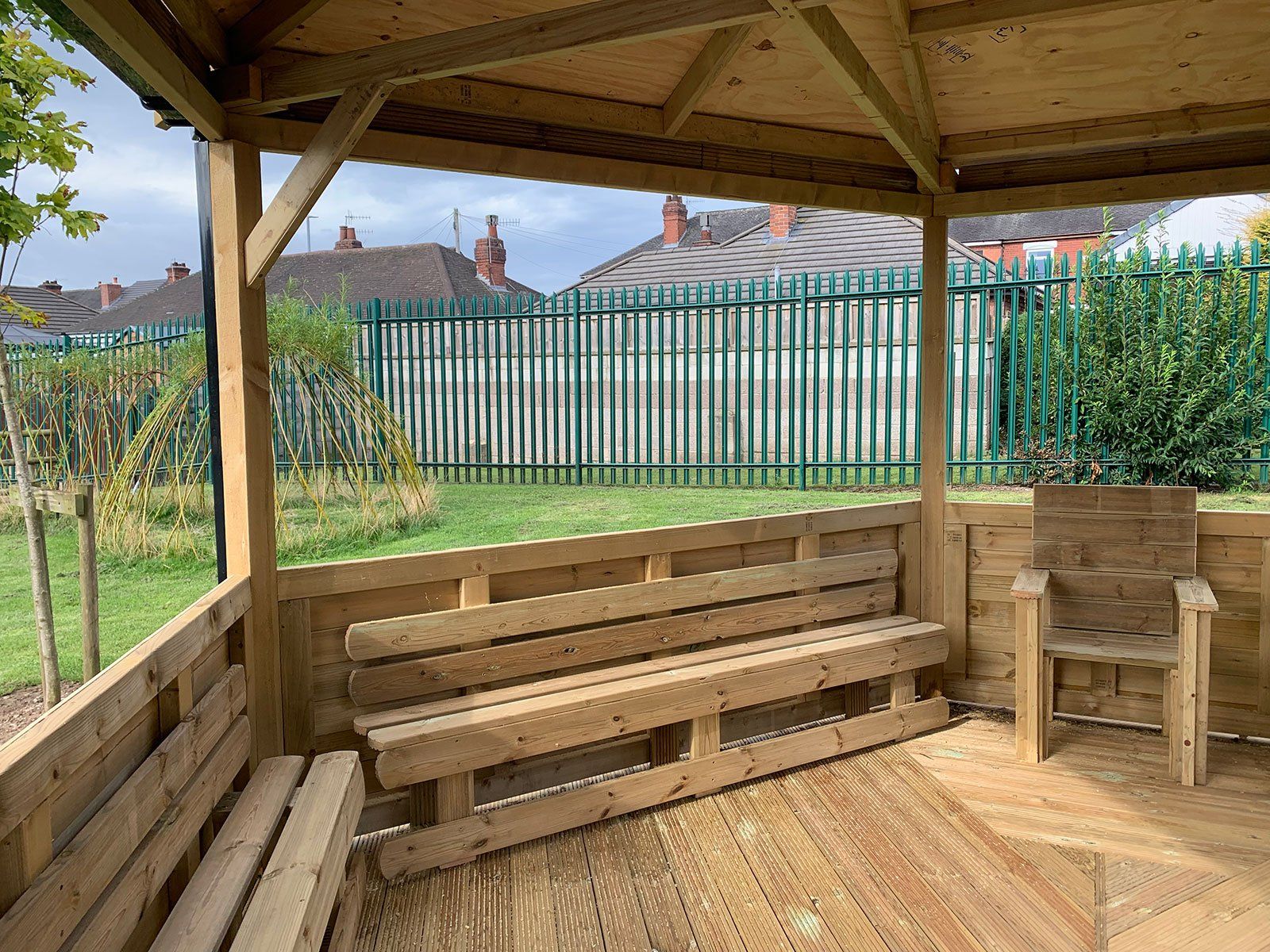 A wooden gazebo with a bench and chairs underneath it.
