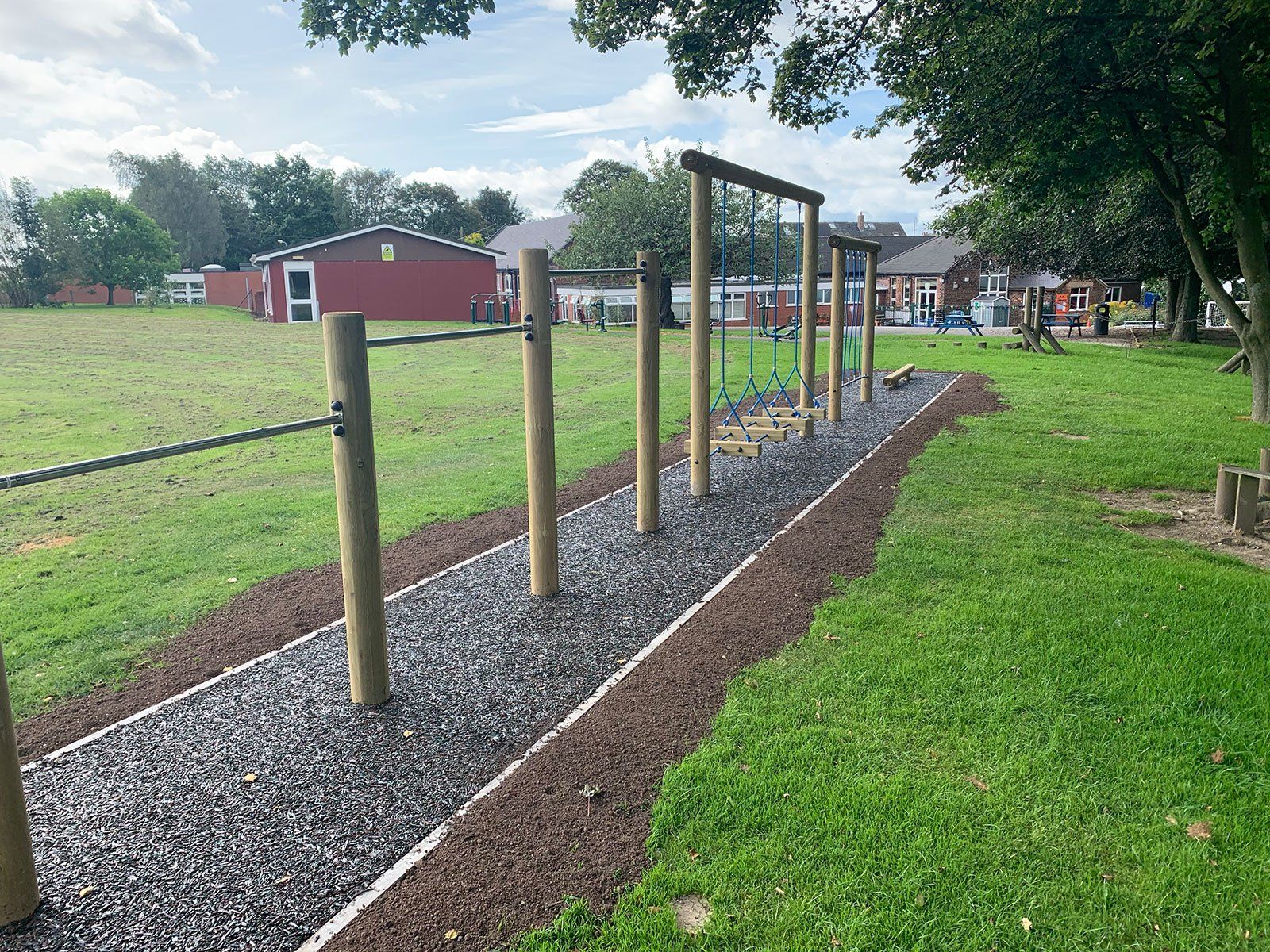 A row of wooden bars in a park with a red barn in the background.