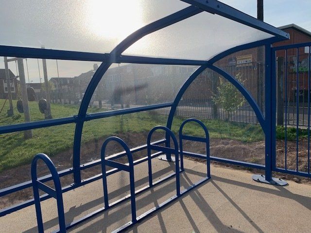A blue bicycle rack with a clear roof in a park.
