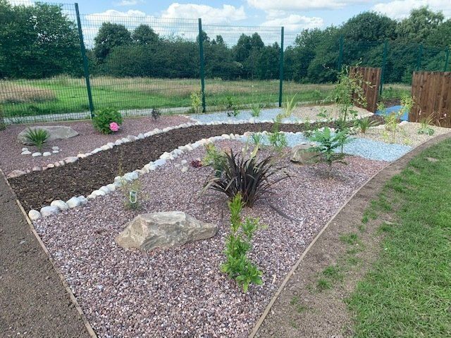 A garden filled with rocks and plants with a fence in the background.