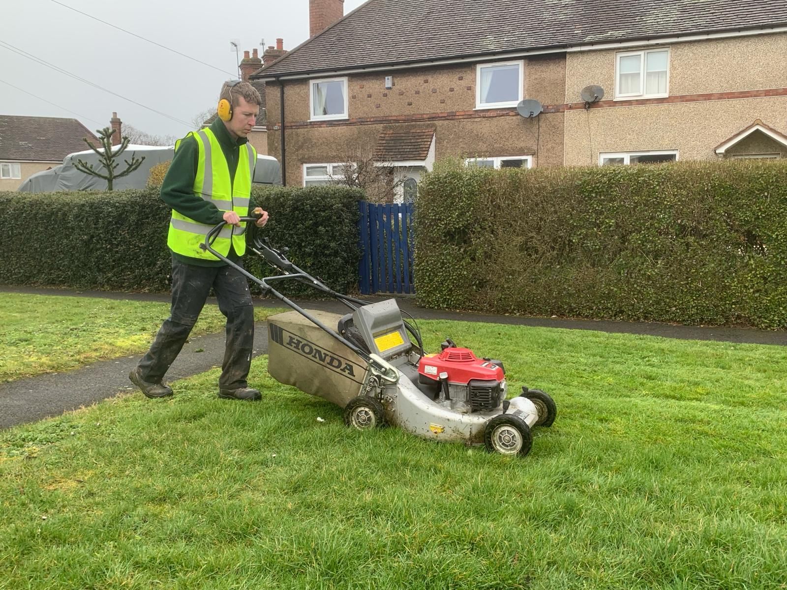 A man is using a lawn mower to cut the grass in front of a house.