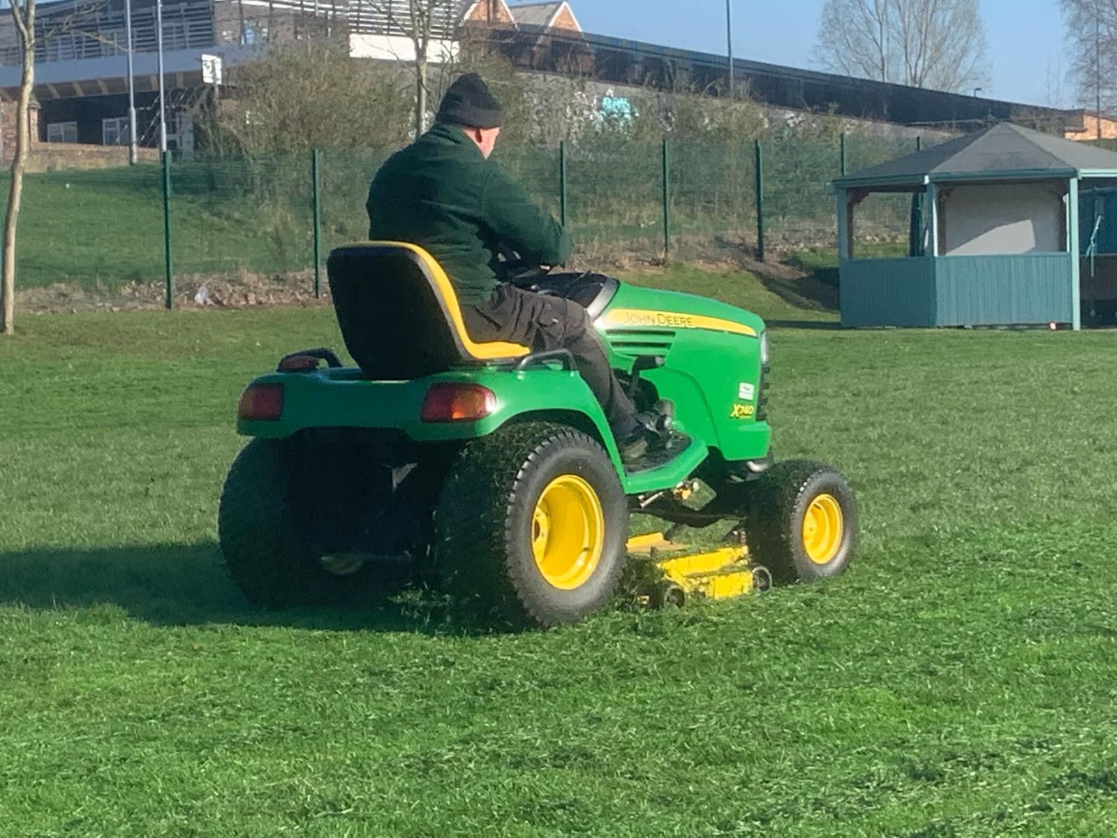 A man is riding a john deere lawn mower on a lush green field.