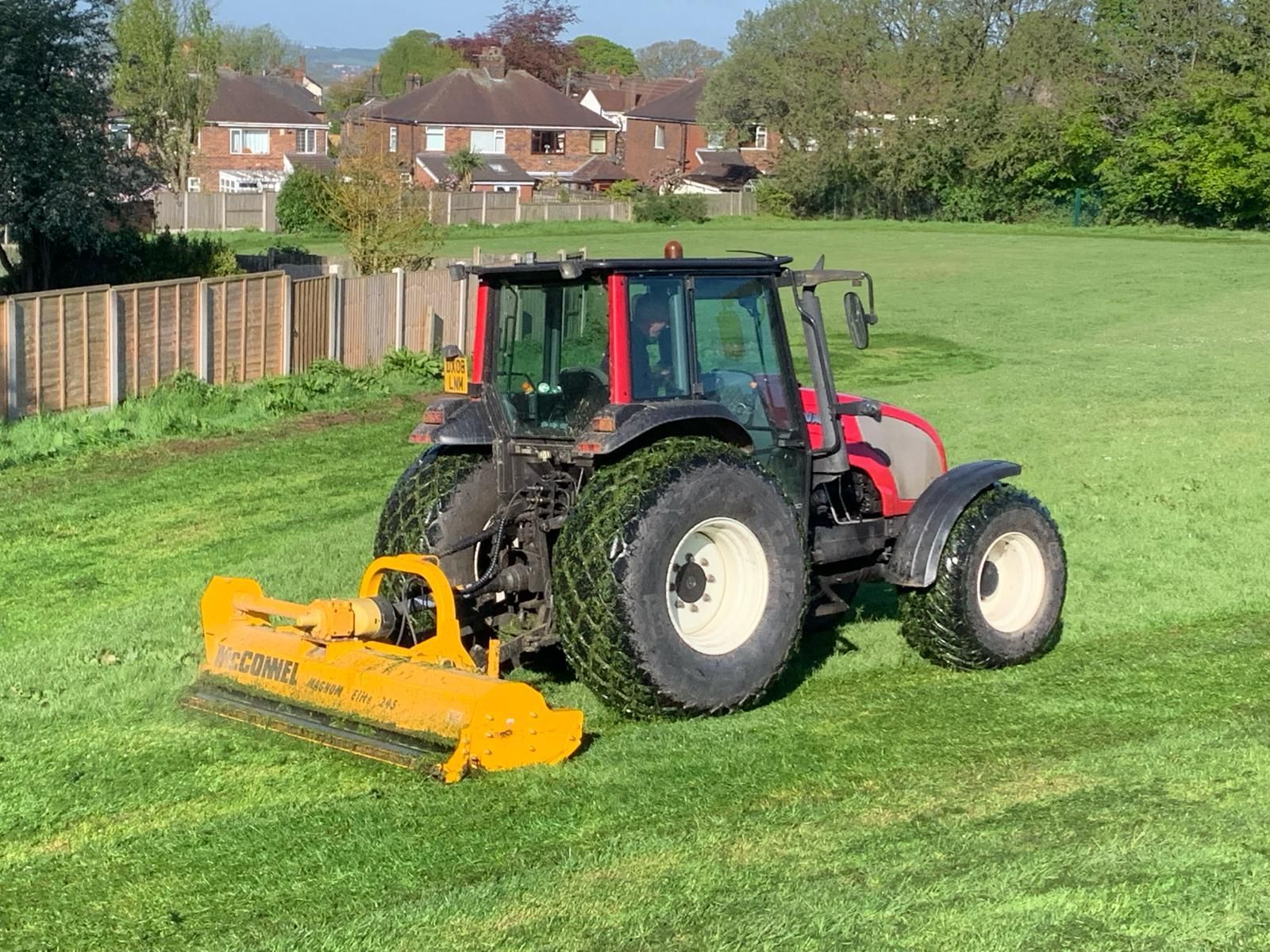 A tractor is cutting grass in a field with a yellow mower.