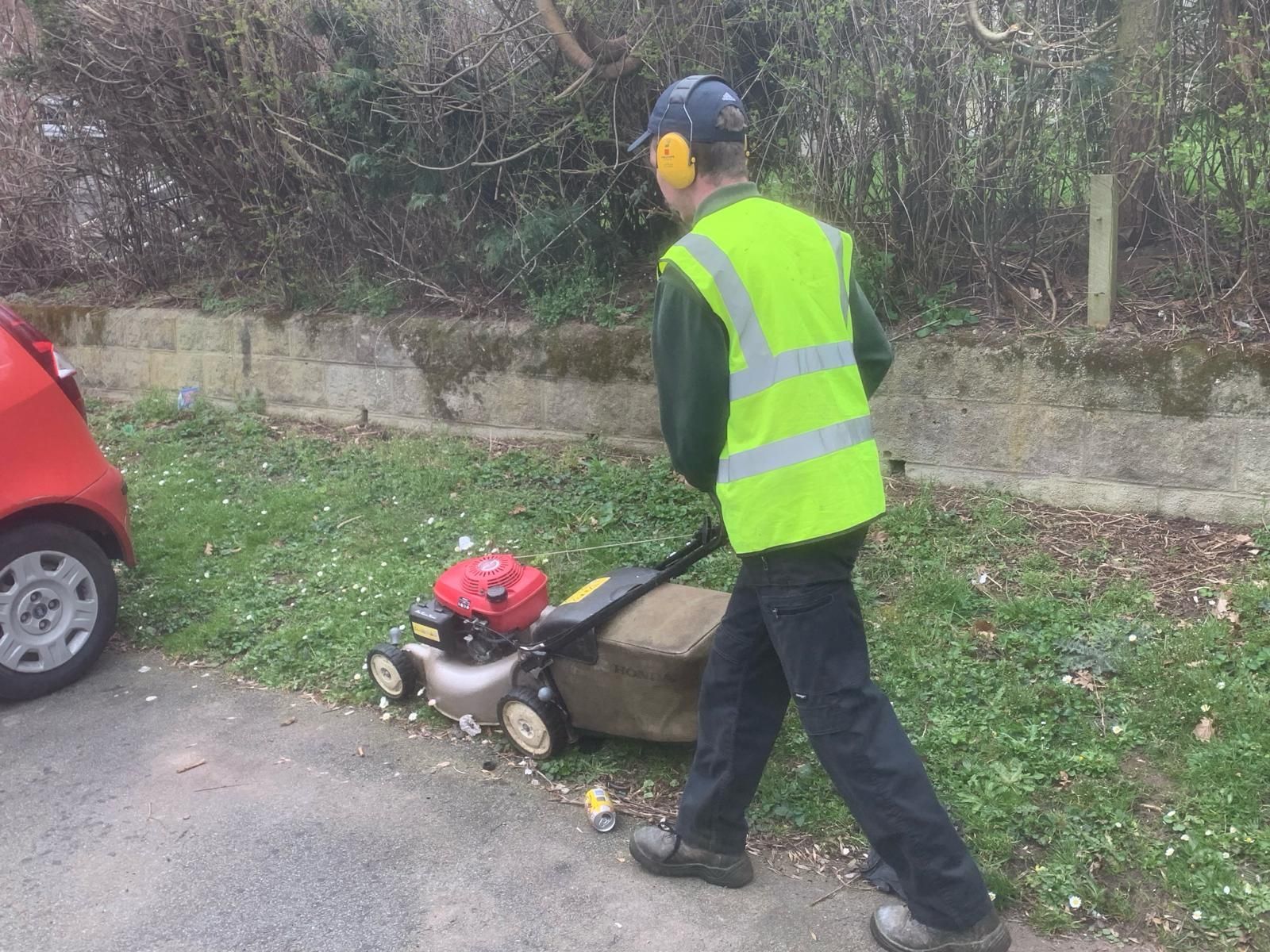 A man in a yellow vest is cutting grass with a lawn mower.