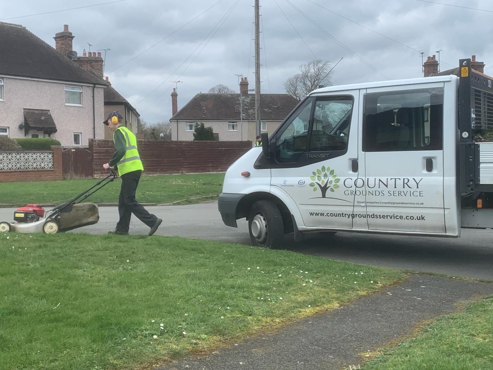 A man is mowing the grass in front of a van.