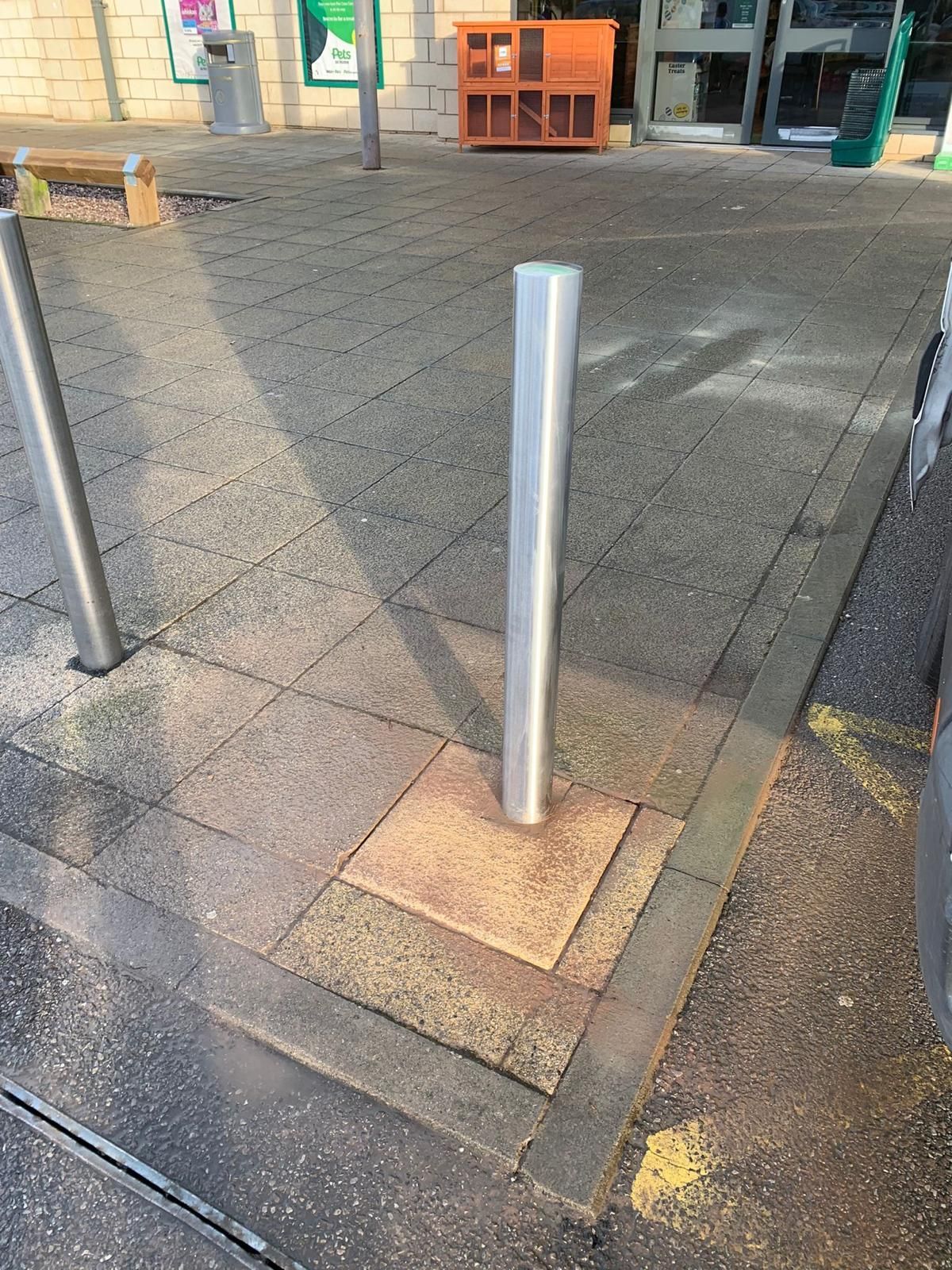 A stainless steel pole is sitting in the middle of a brick pavement.