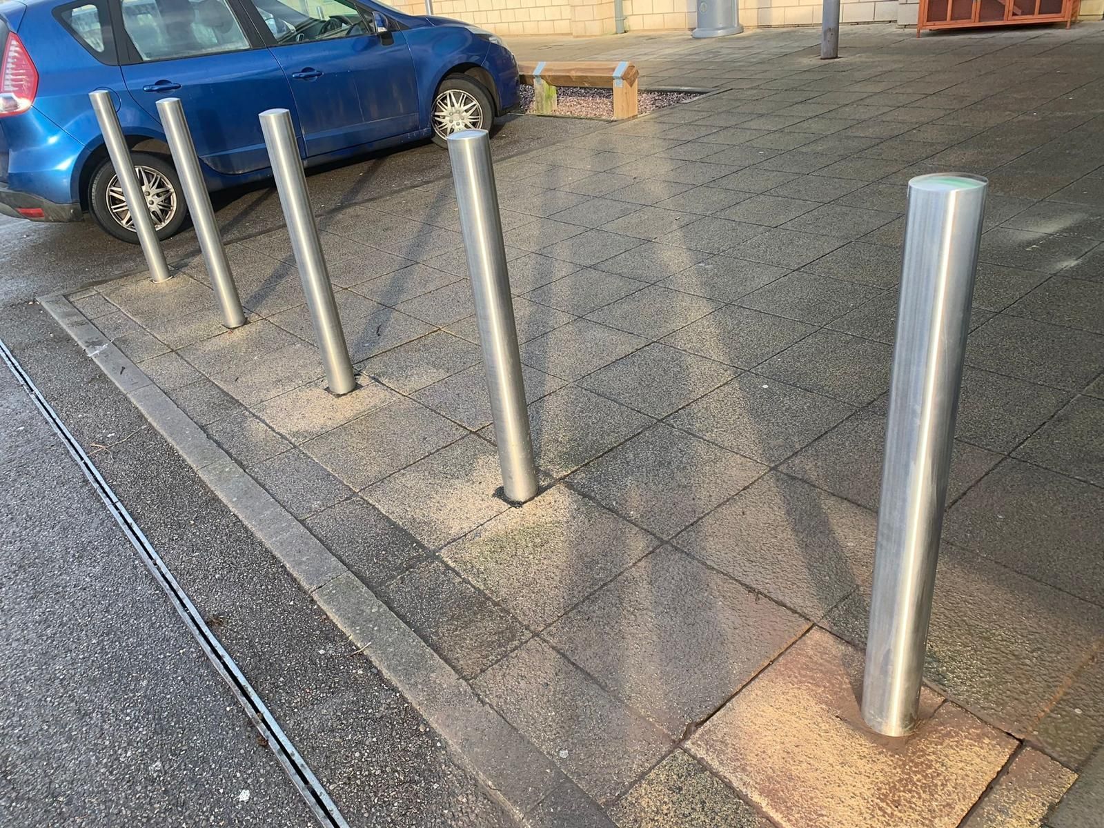 A blue car is parked next to a row of metal poles.