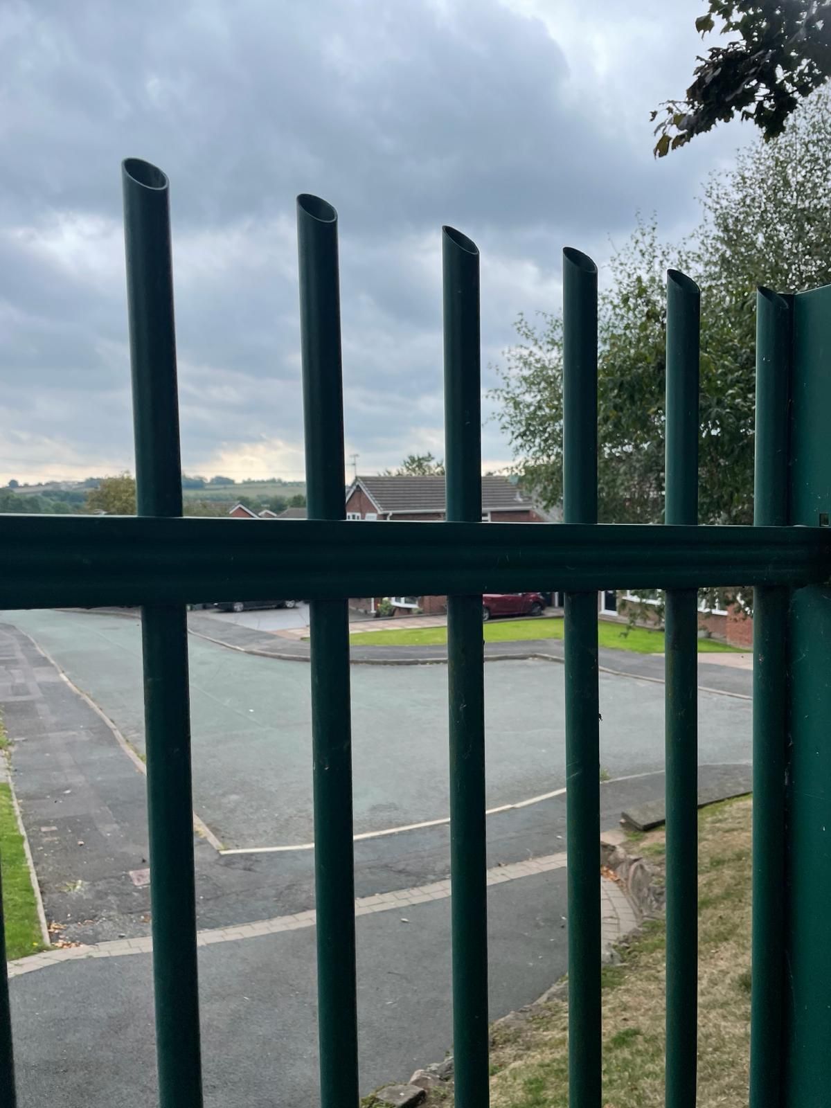 A green fence is surrounding a parking lot with a house in the background