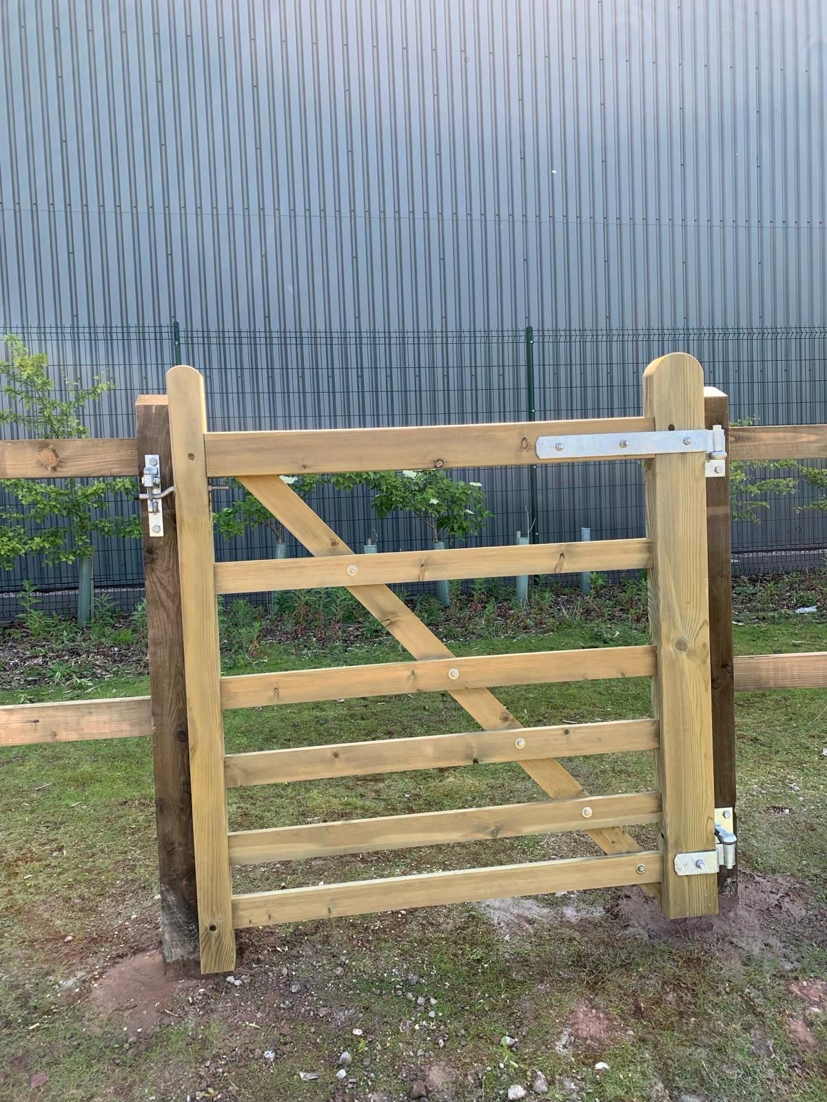 A wooden gate is sitting in the grass next to a fence.