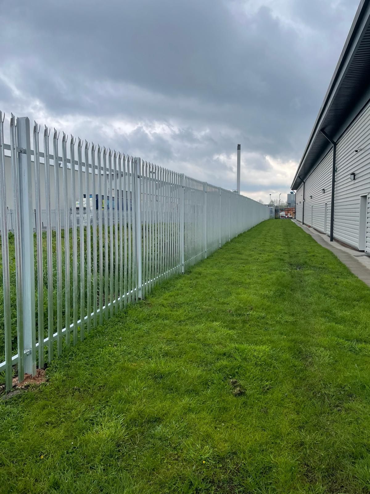 A long metal fence surrounds a lush green field next to a building.