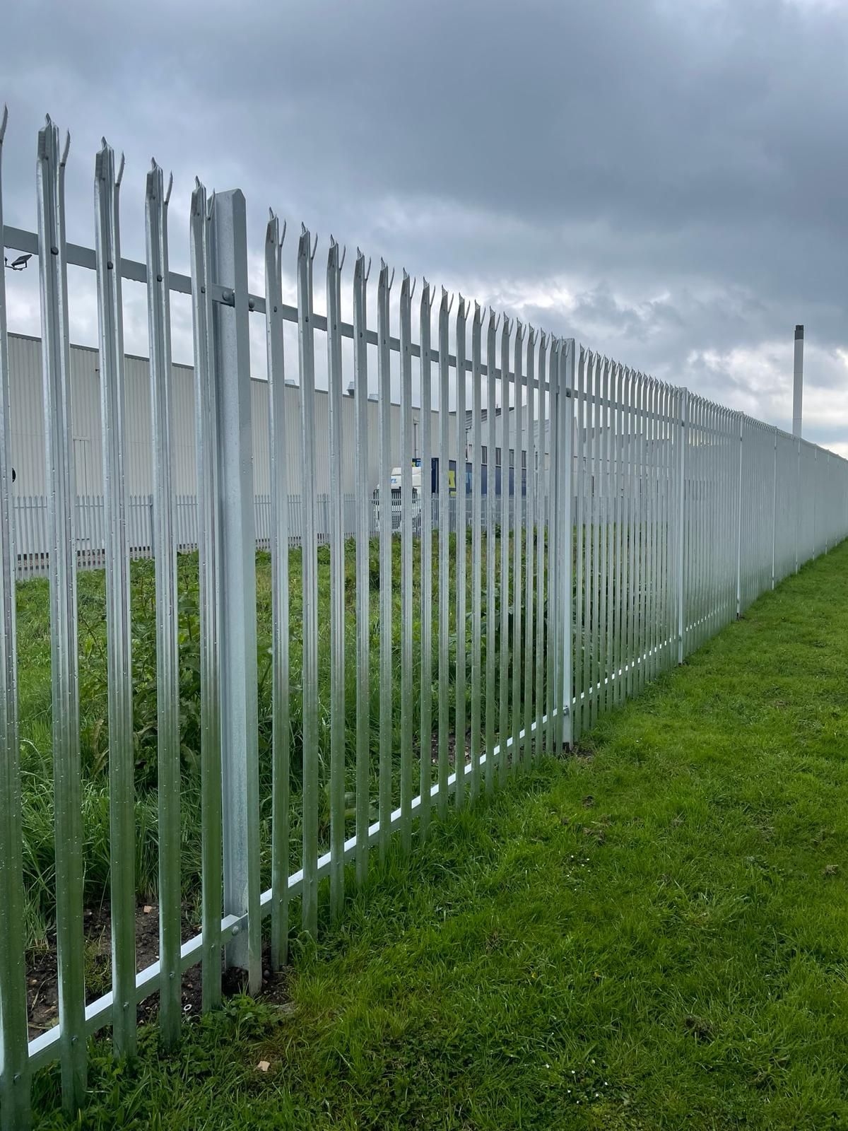 A long metal fence surrounds a lush green field.