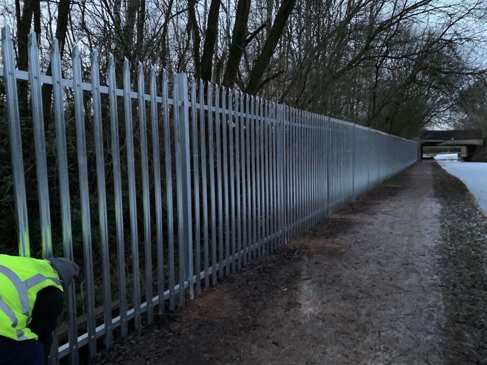 A man in a yellow vest is working on a metal fence.