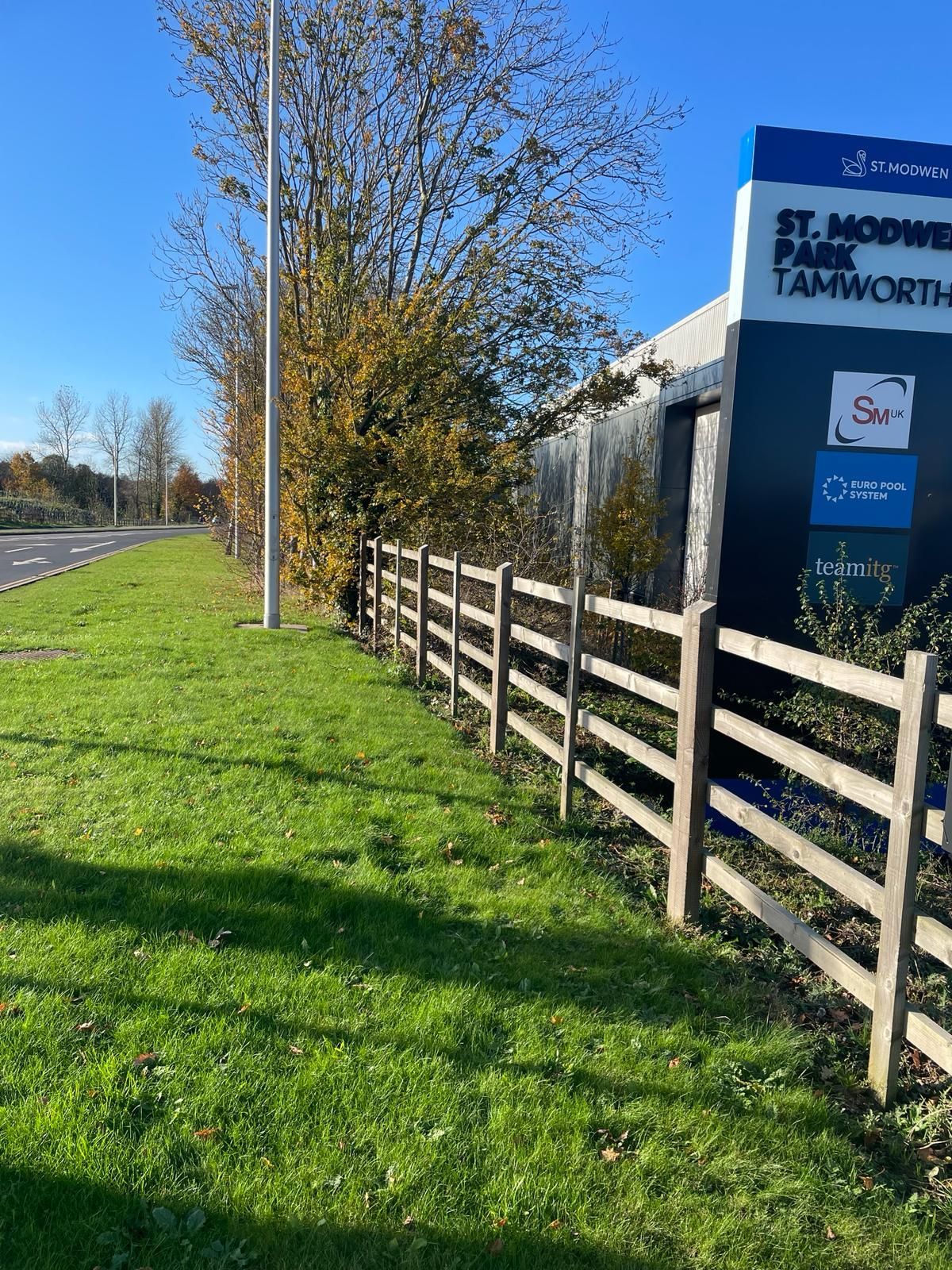 A wooden fence surrounds a grassy field next to a road.