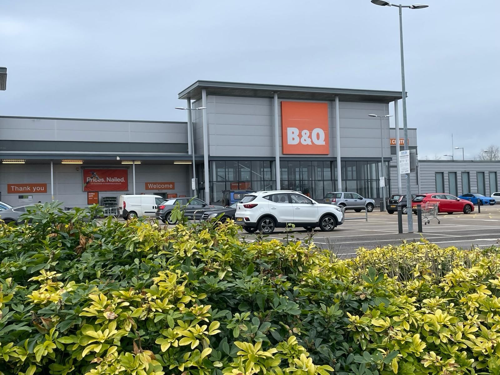 A white car is parked in front of a b & q store.