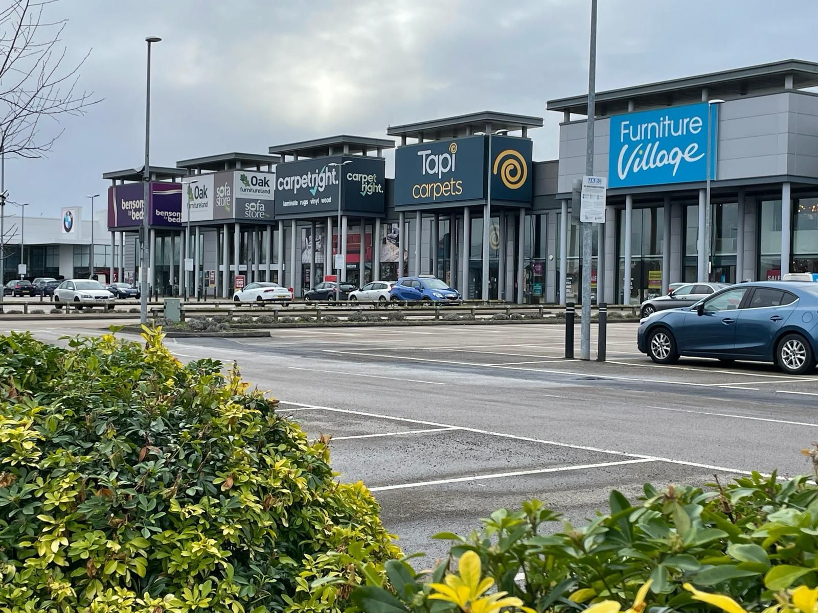 A blue car is parked in front of a furniture village store.