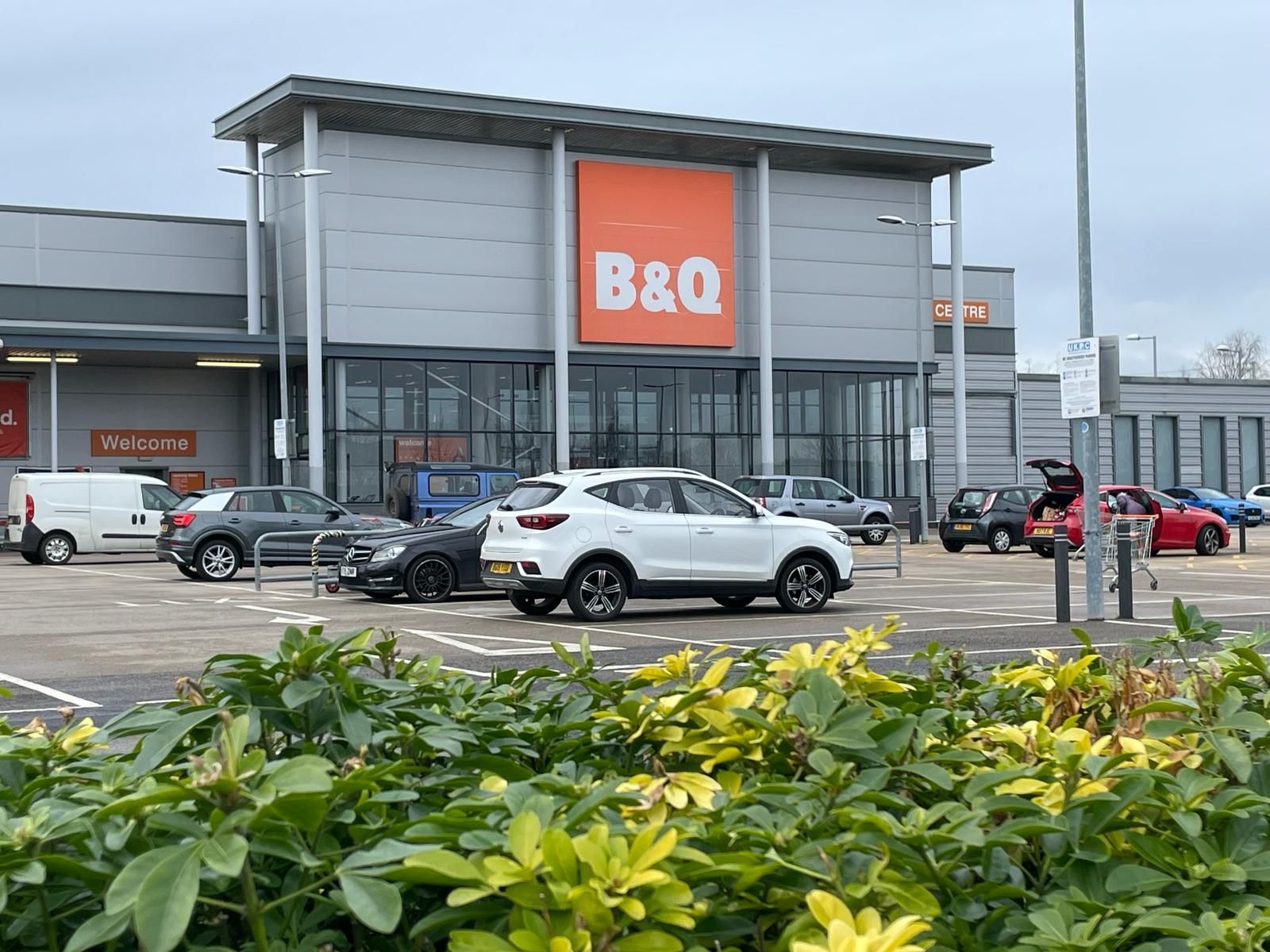 A white suv is parked in front of a b & q store.