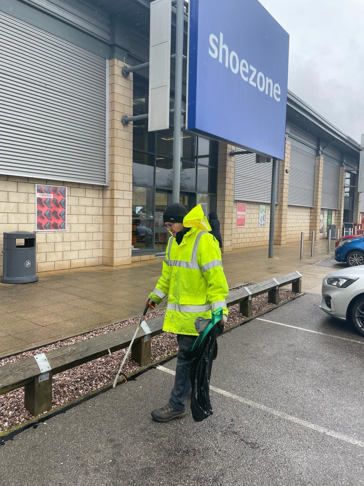 A man in a yellow jacket is standing in front of a shoezone store.