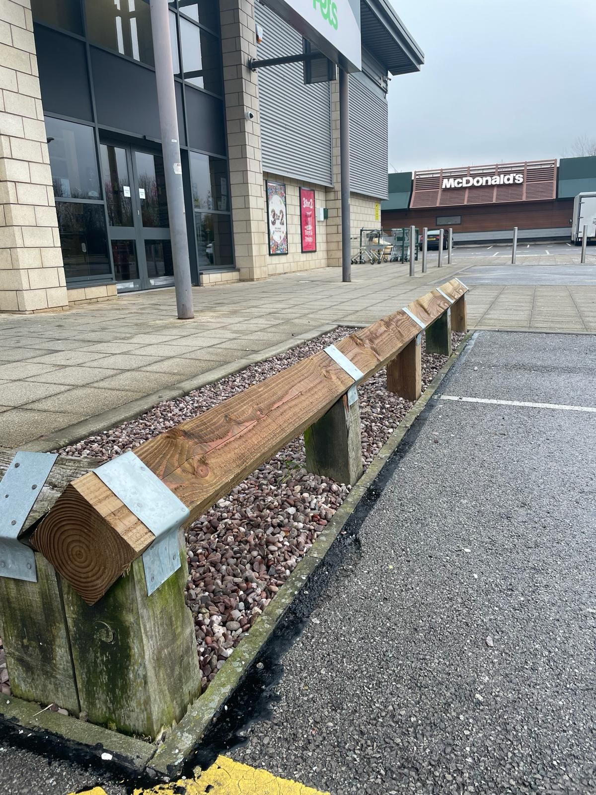 A wooden bench is sitting in front of a building in a parking lot.