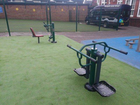 A playground with a bench and exercise equipment and a van parked in the background.