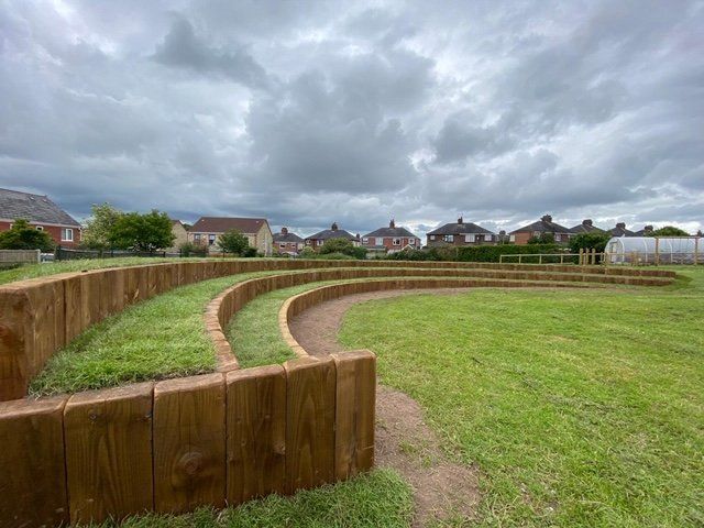 A wooden amphitheater in a park with a cloudy sky in the background.