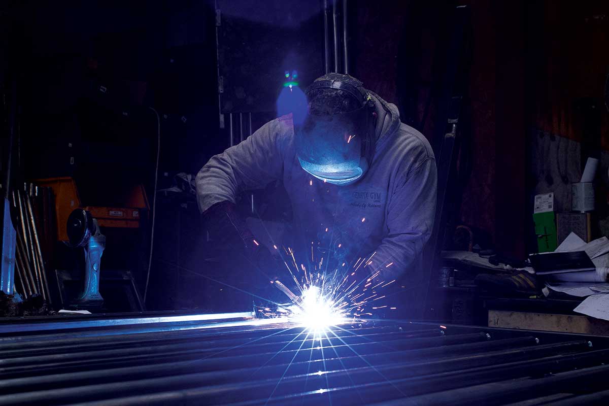 A man is welding a piece of metal in a dark room.