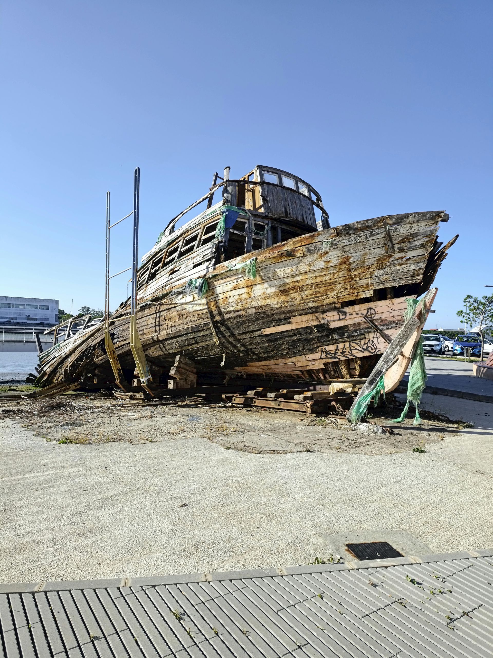 An old rusty boat is sitting on the ground in a parking lot.