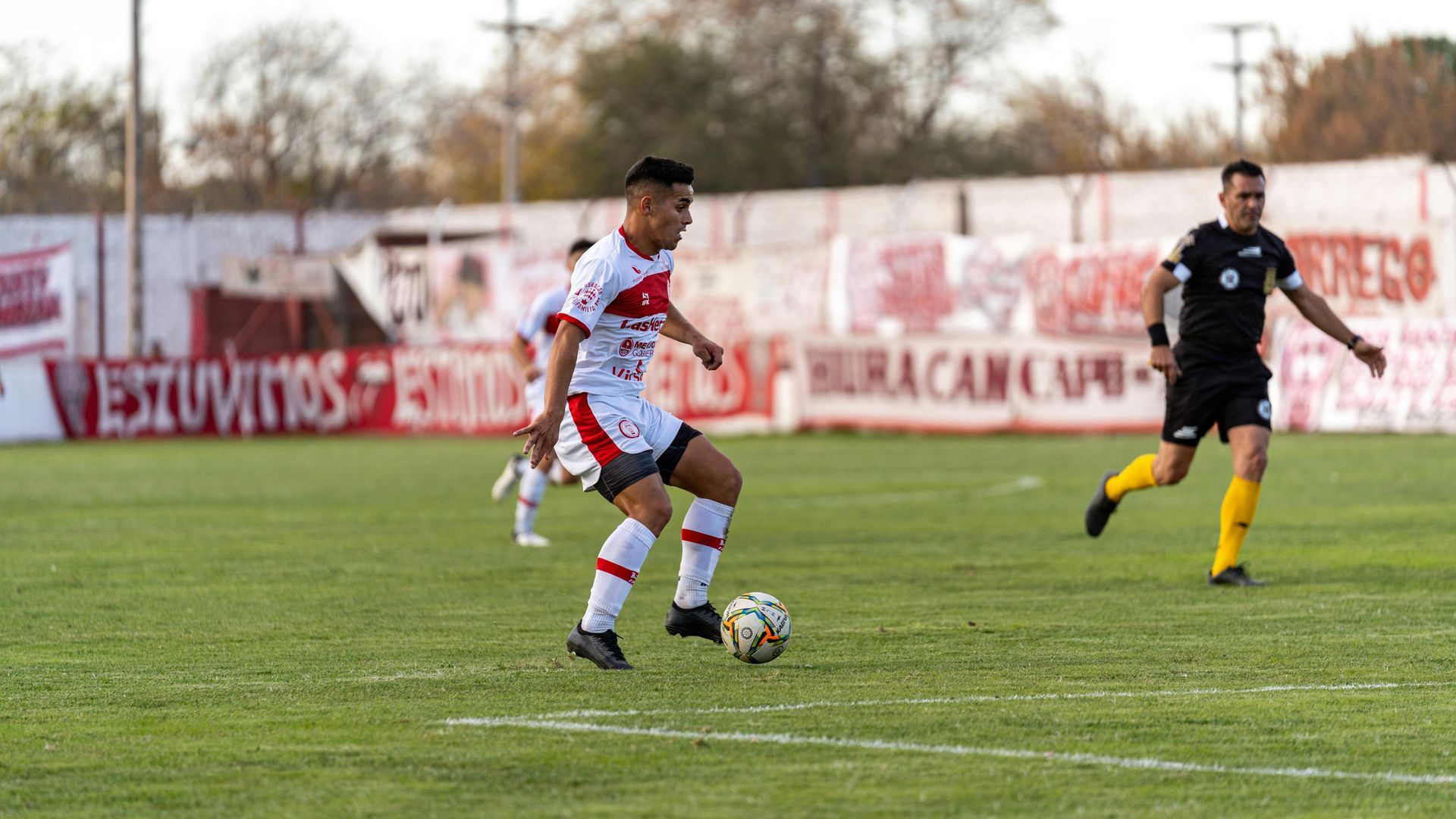 A man is kicking a soccer ball on a field while another man watches.
