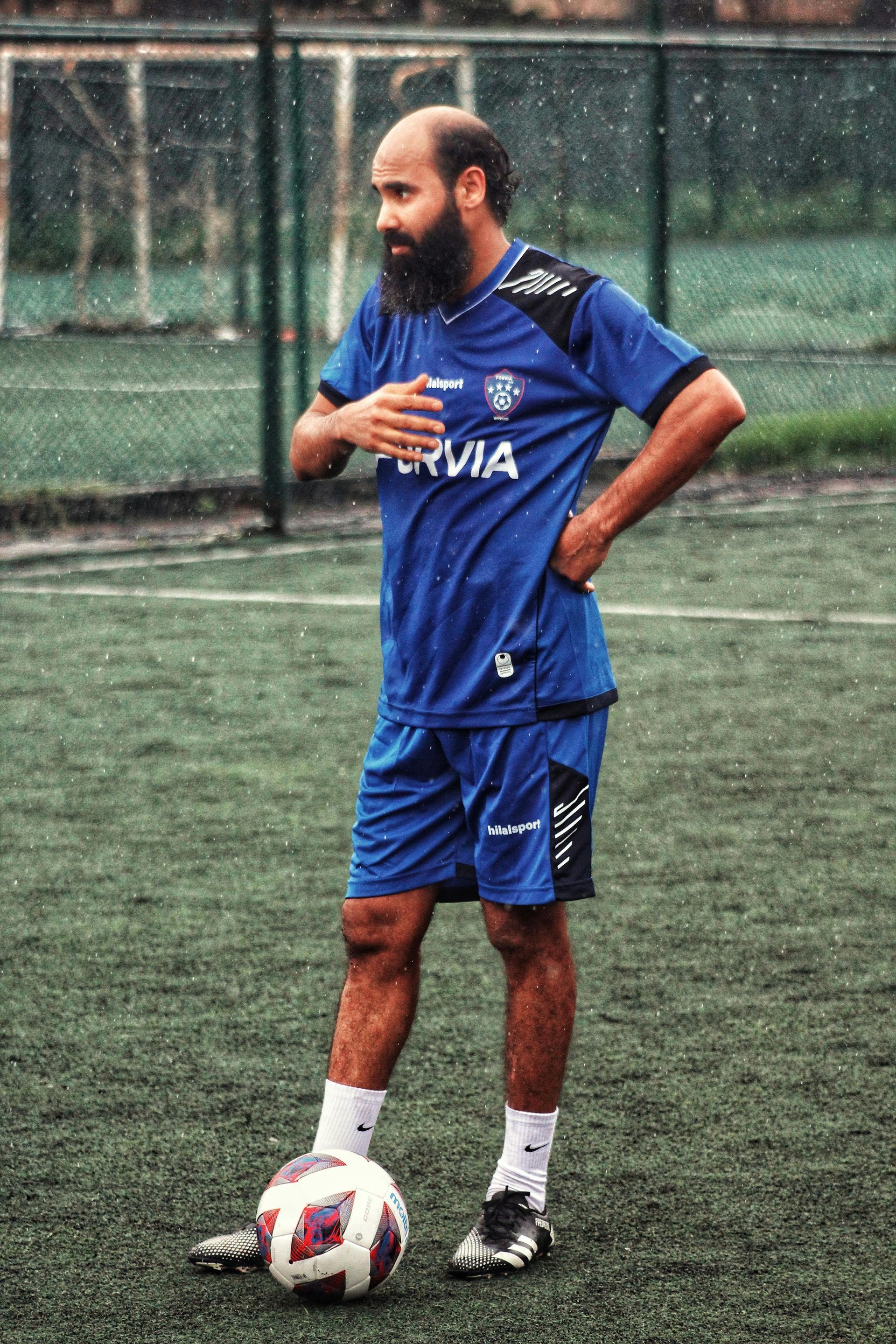 A man with a beard is standing next to a soccer ball on a field.
