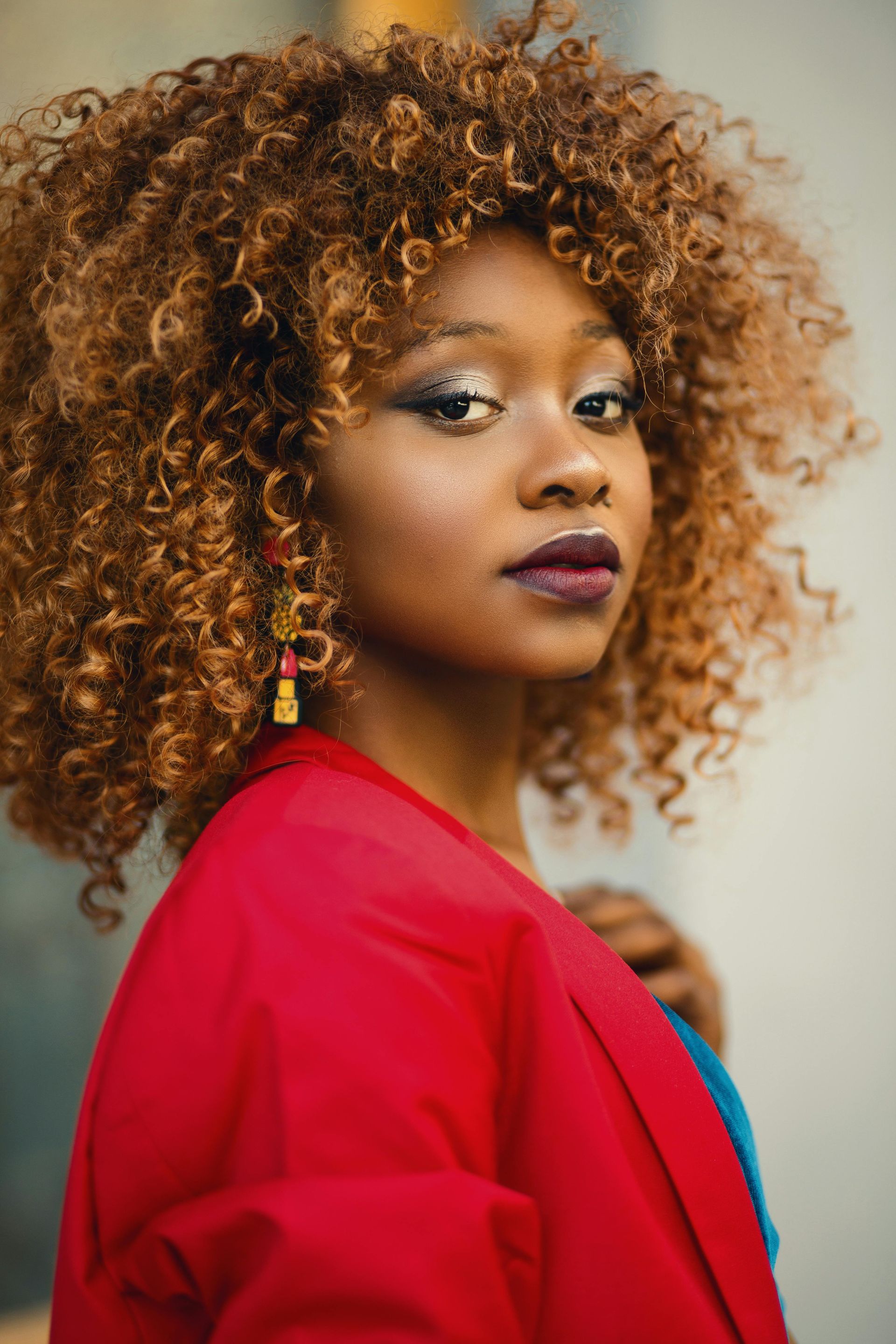 A woman with curly hair is wearing a red jacket and earrings.
