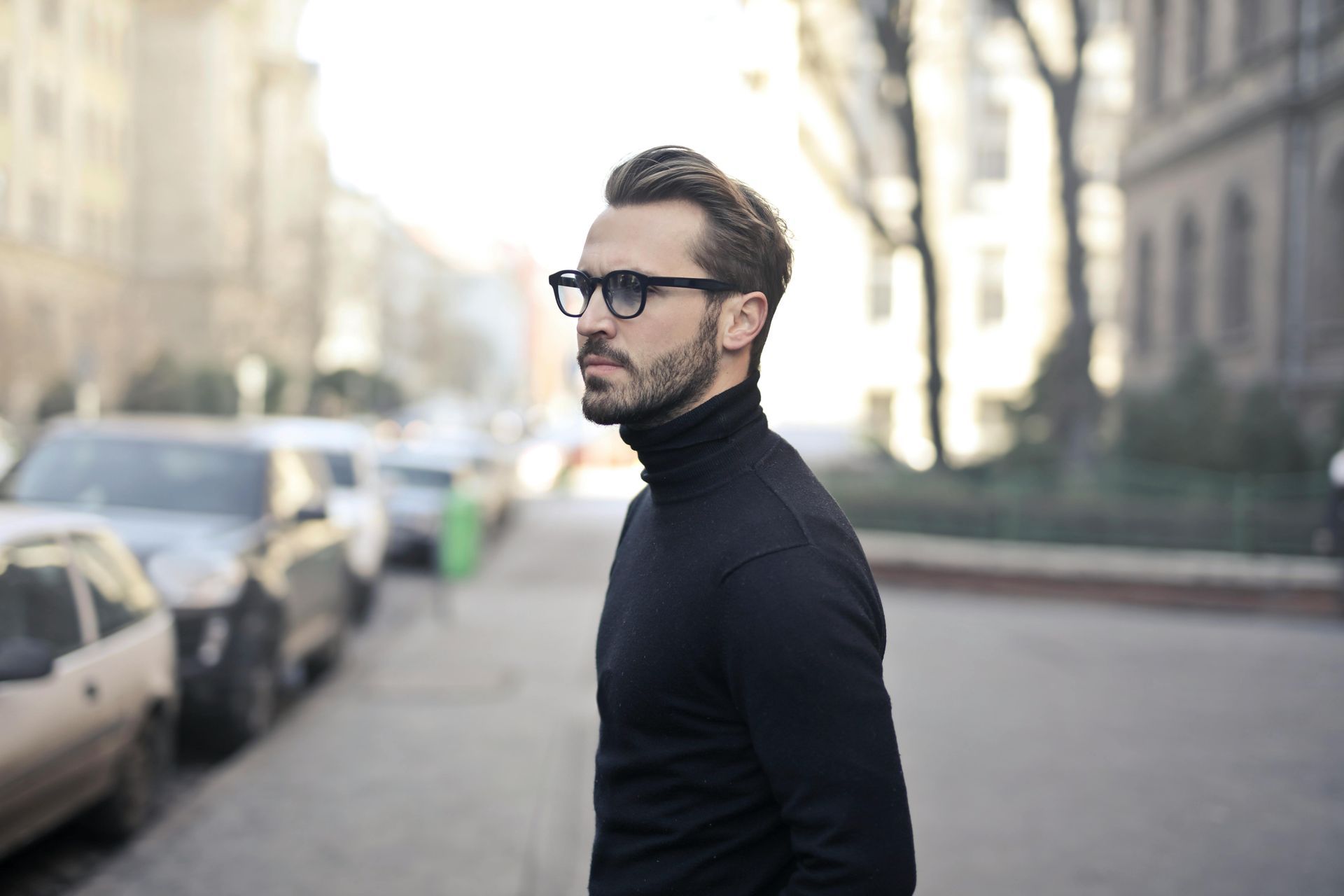 A man wearing glasses and a black turtleneck is walking down a street.
