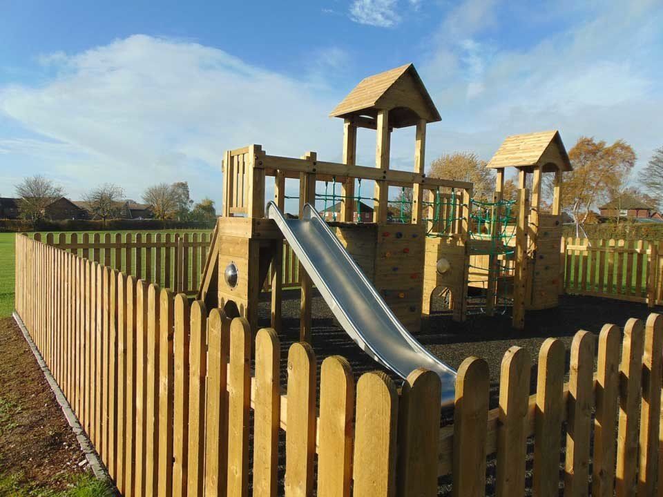 A wooden playground with a slide surrounded by a wooden fence.