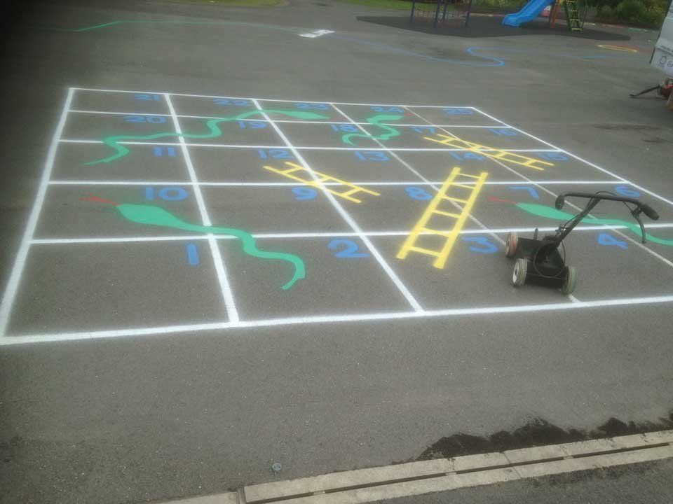 A lawn mower is sitting next to a snake and ladder game painted on the ground