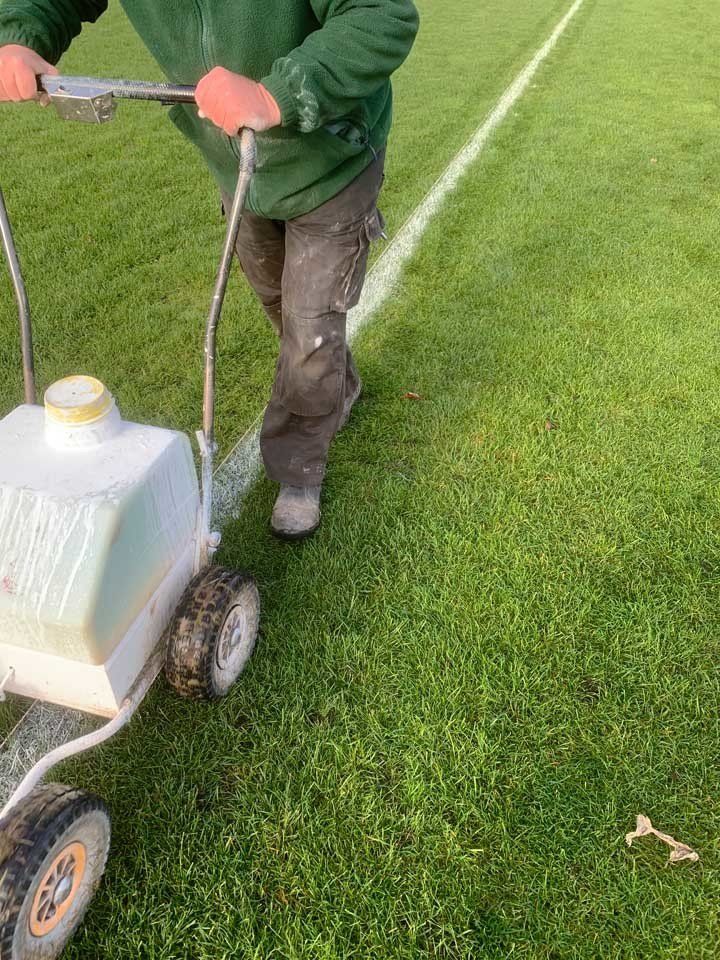 A man is using a machine to paint a line on a soccer field.