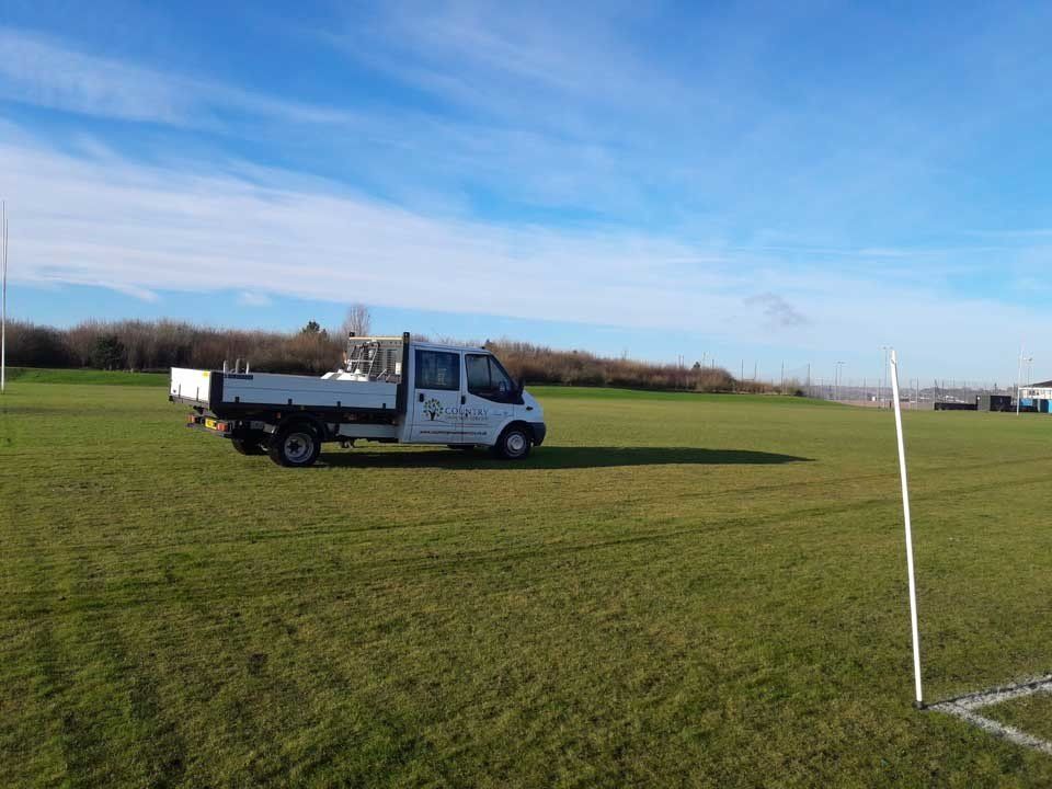 A white truck is parked in a grassy field next to a soccer goal.