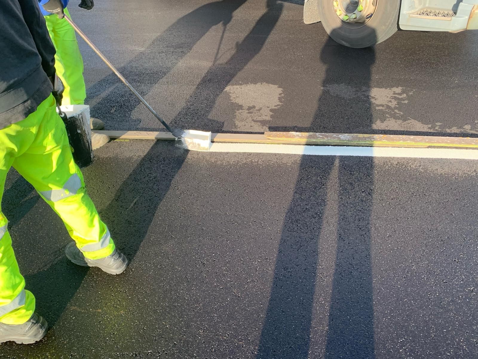 A man in yellow pants is painting a line on the road.