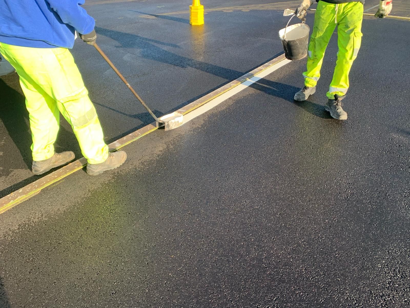 A man is using a broom to spread asphalt on a road.