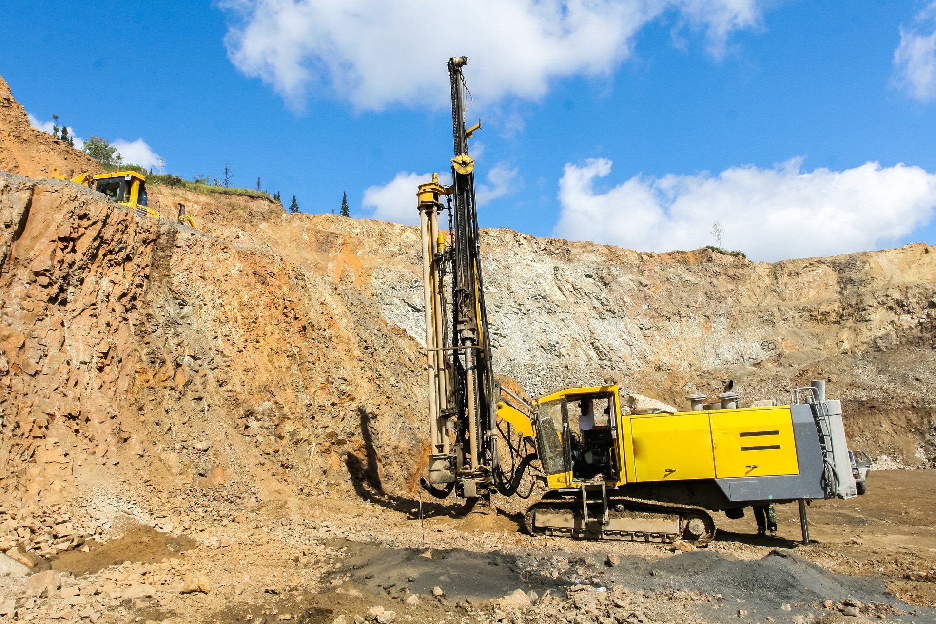 Yellow Drill Rig Working on a Rock Quarry Face Under a Blue Sky — Wilson's Drilling in Moore Park Beach, QLD