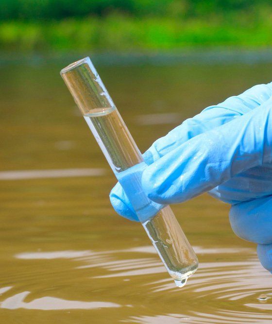 Gloved Hand Holding a Clear Water Sample Vial Near a Body of Water — Wilson's Drilling in South Kolan, QLD