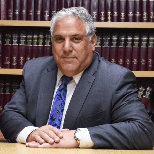 A man in a suit and tie is sitting in front of a bookshelf