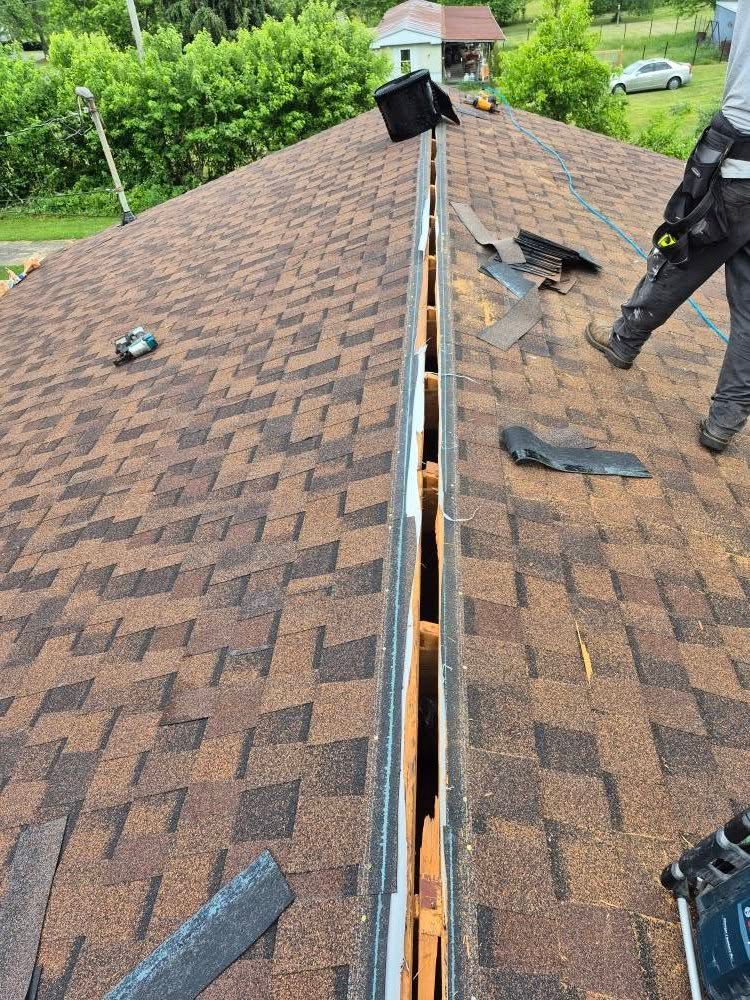 Roofer repairing a roof valley with brown shingles. The setting is outdoors on a sunny day.