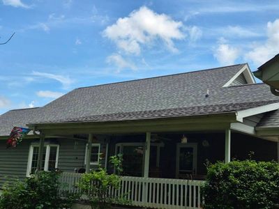 House with dark gray shingle roof, green siding, white porch, and blue sky.