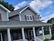 Gray house with white porch, red shutters, and a blue sky.