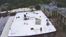 Rooftop workers on a commercial building. Buildings and trees in the background.