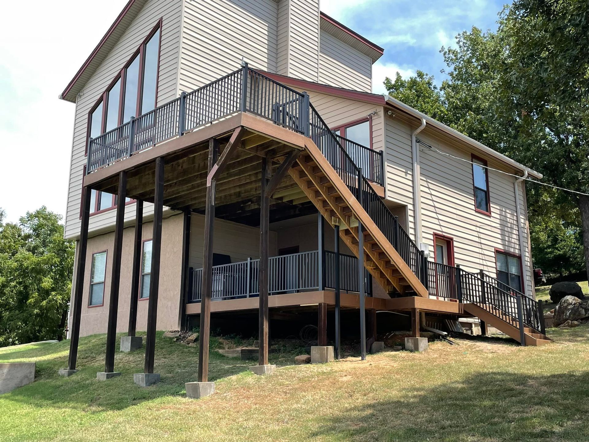 Two-story house with a wooden deck and stairs. Beige siding, brown deck and railing, green grass.
