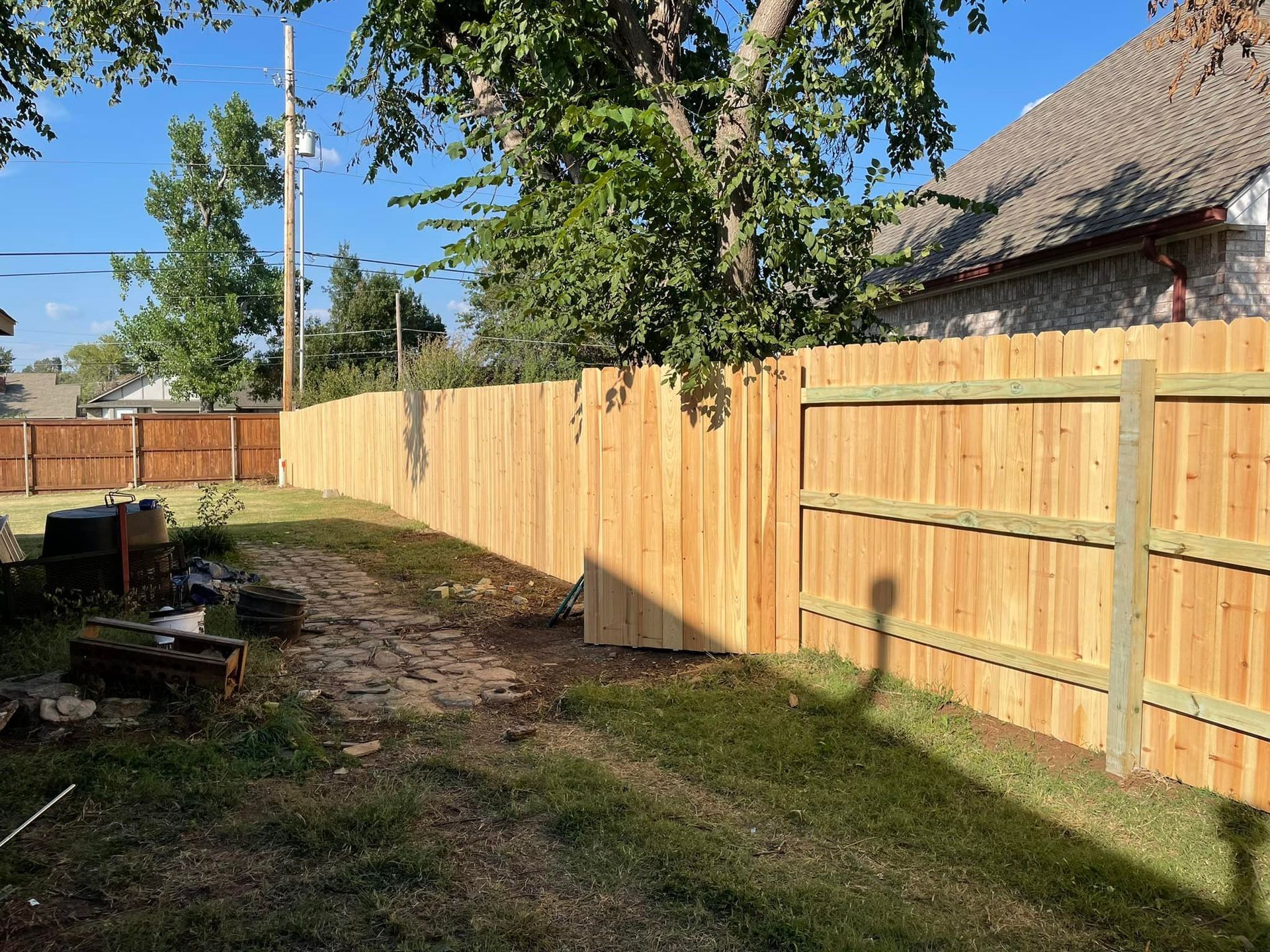 Wooden fence in a backyard with green grass and a clear blue sky.